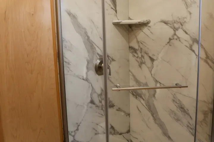 Compact bathroom with corner shower, glass door, marble walls, and adjacent toilet.