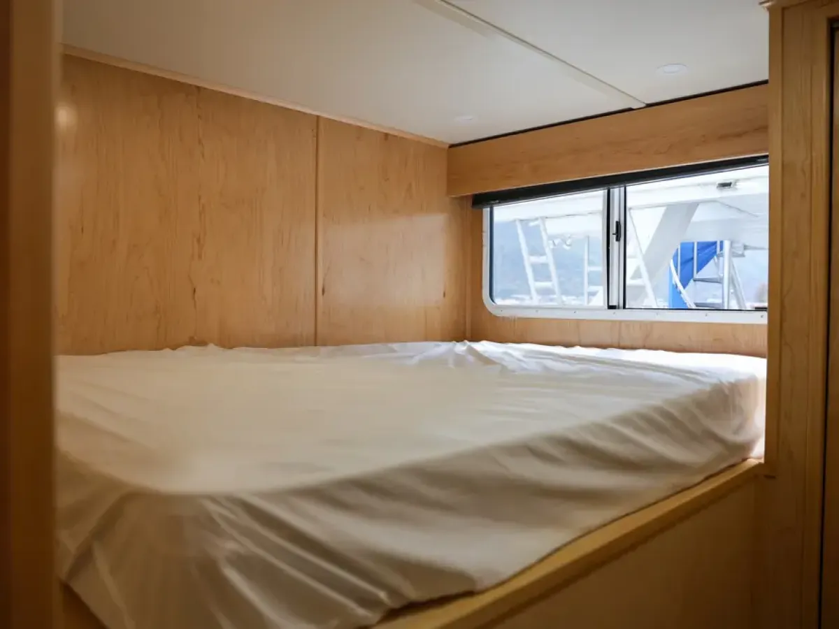 Compact wooden bedroom with a neatly made bed and a window.