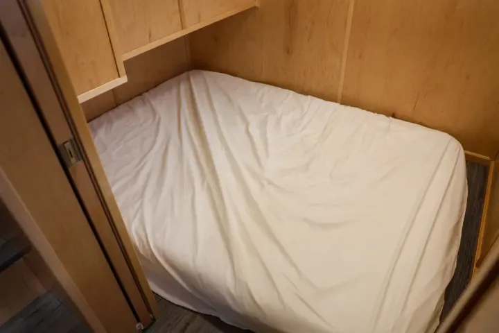 A small wooden room with a single bed covered in a white sheet.