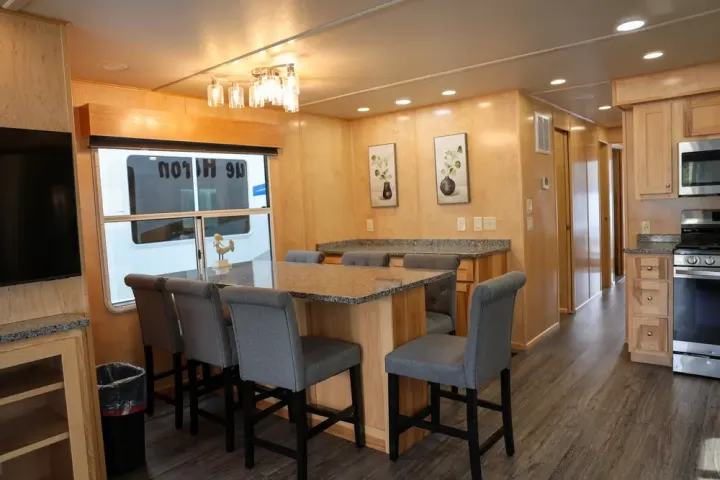 Modern RV interior with dining area, gray chairs, and built-in kitchen cabinets.