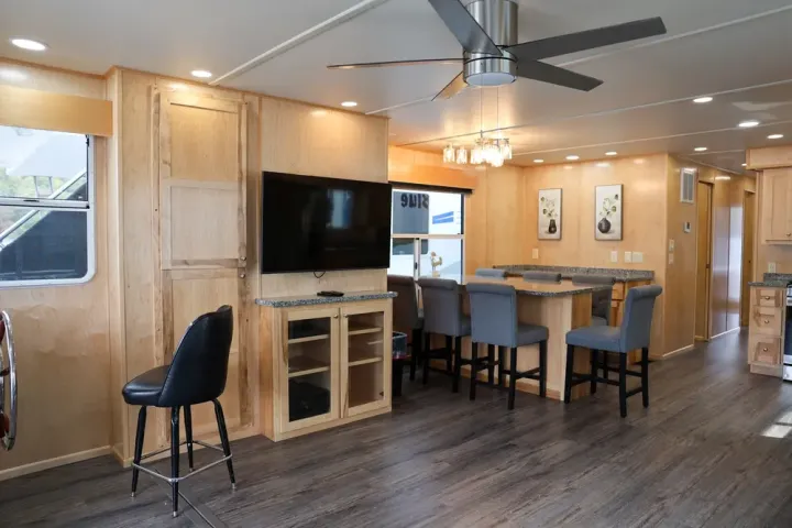Modern RV interior with wood paneling, TV, dining area, barstools, and ceiling fan.