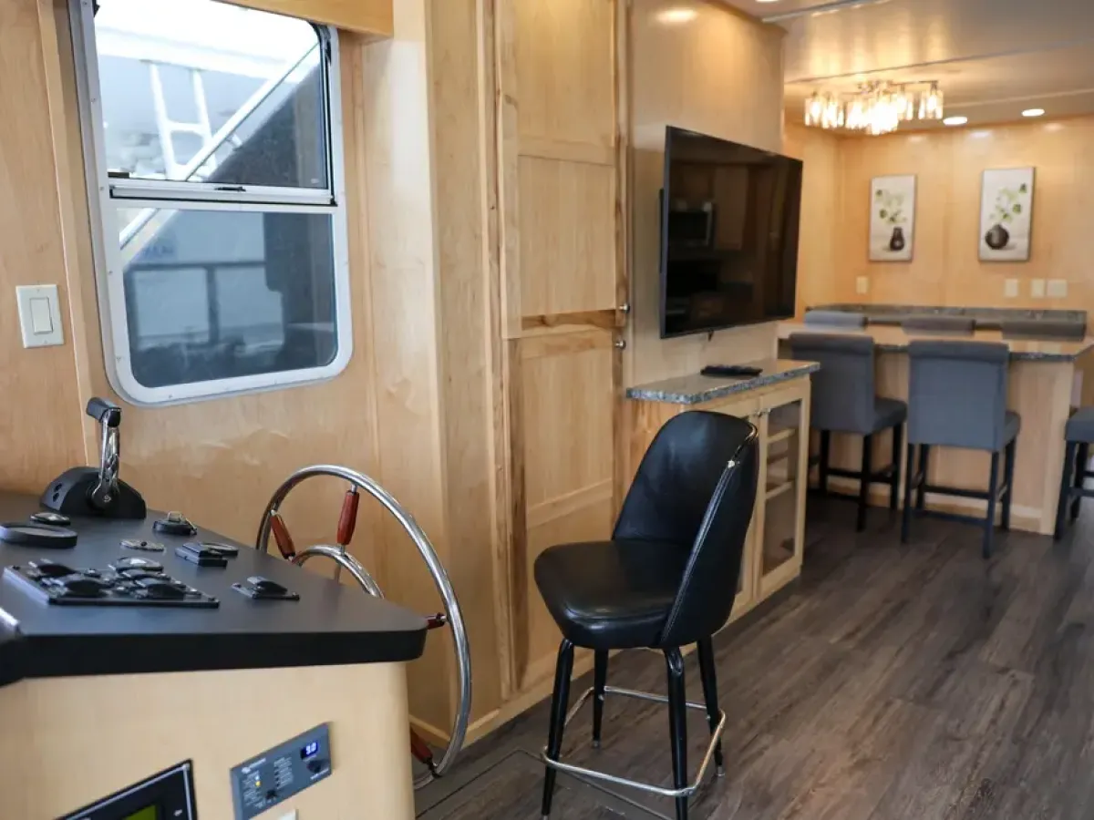 Interior of a modern RV with a steering wheel, TV, and dining area with bar stools.