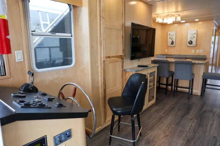 Interior of a modern RV with a steering wheel, TV, and dining area with bar stools.