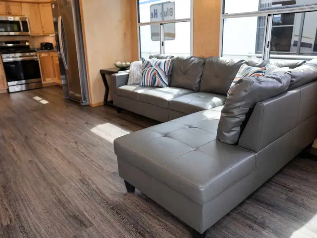 Modern kitchen and living area with gray sectional sofa and wooden cabinets.