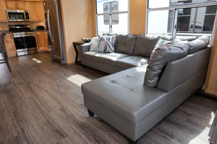 Modern kitchen and living area with gray sectional sofa and wooden cabinets.