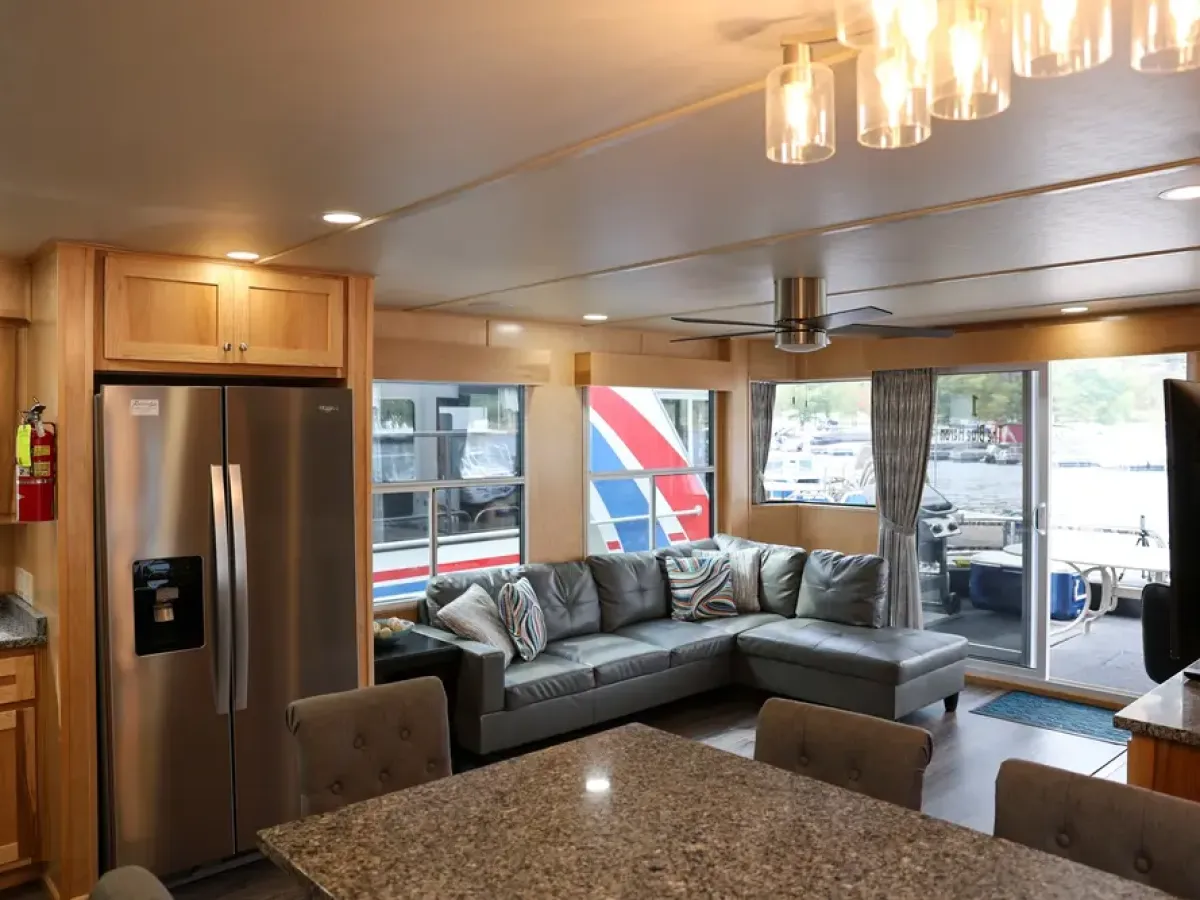 Modern kitchen and living area on a houseboat with stainless steel appliances and large windows.