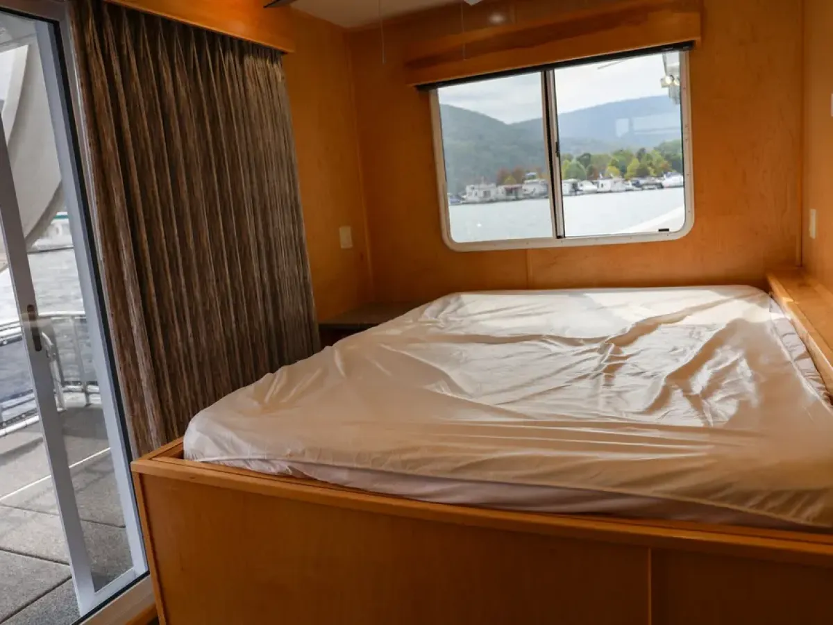 Interior of a room on a boat with a bed, curtained window, and view of water.