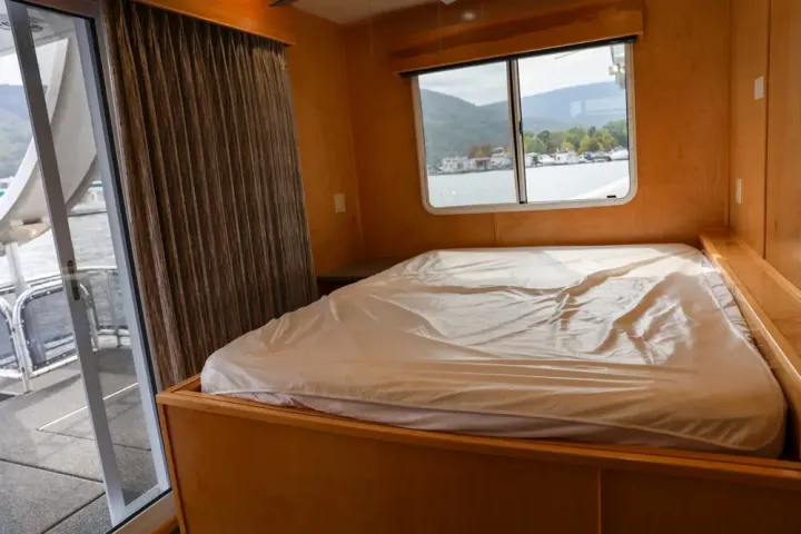 Interior of a room on a boat with a bed, curtained window, and view of water.