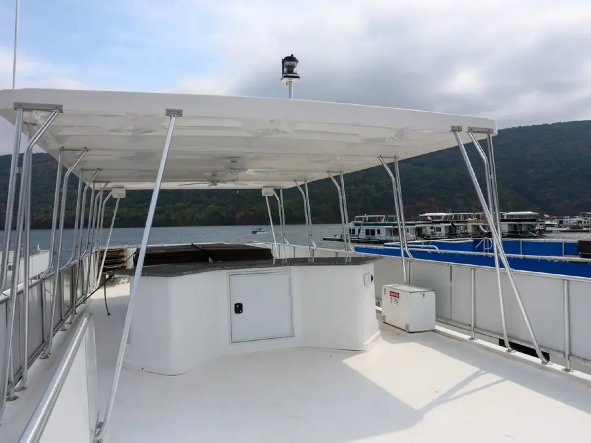 A boat's upper deck with a covered seating area, surrounded by water and hills.