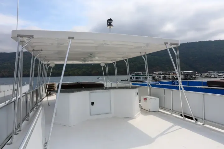 A boat's upper deck with a covered seating area, surrounded by water and hills.