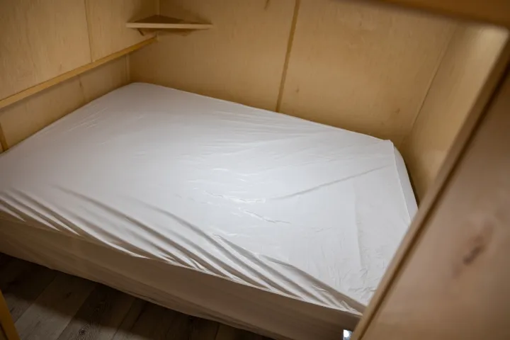 Small room with a neatly made bed and wooden walls.