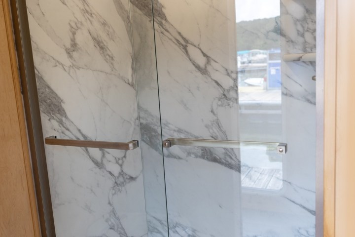 Modern shower with glass doors and marble-patterned walls.