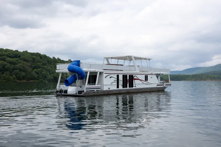 Houseboat with a blue slide on a lake surrounded by hills.