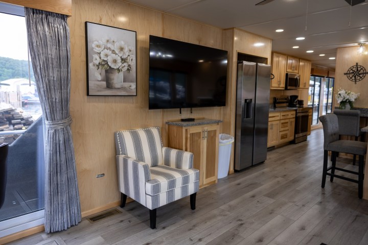Modern RV interior with TV, striped chair, and kitchen appliances.