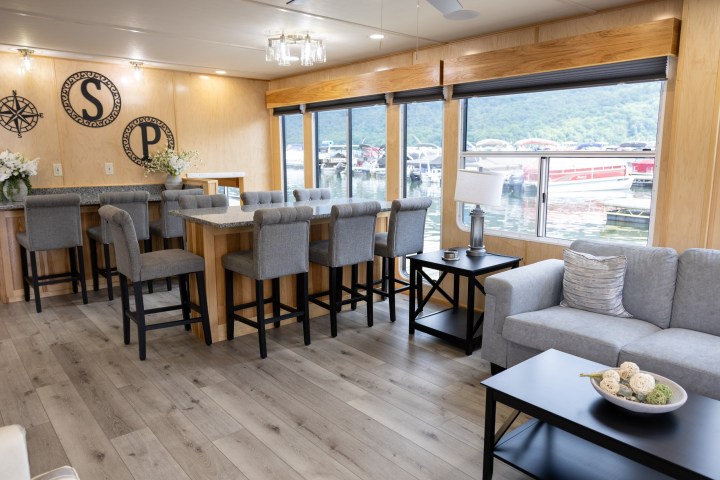 Modern living area with bar, gray seating, and large windows overlooking a marina.